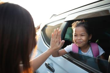 Elementary student waving goodbye through car window